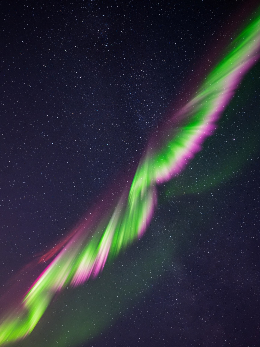 A ribbon of green and magenta aurora cutting through a star field.